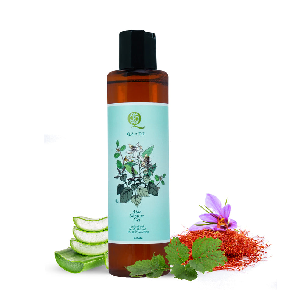 The image shows a bottle of Qaadu Aloe Shower Gel. The bottle has a light blue label featuring botanical illustrations. The text on the label indicates it is infused with aloe, pink basil oil, and other ingredients. The bottle is surrounded by aloe slices, pink basil leaves, and saffron.